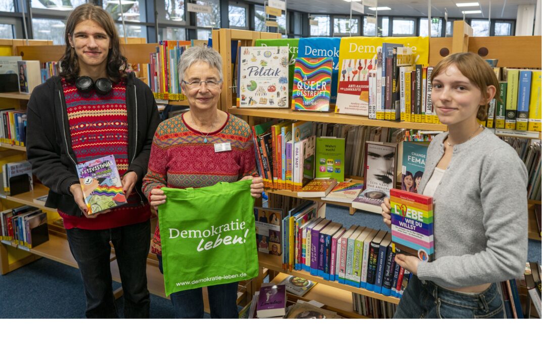 Auf dem Bild sind die Leitung der Stadtbücherei Brunsbüttel und zwei Jugendliche zu sehen, die die Bücher für das Demokratie- und Vielfaltsregal ausgewählt haben.