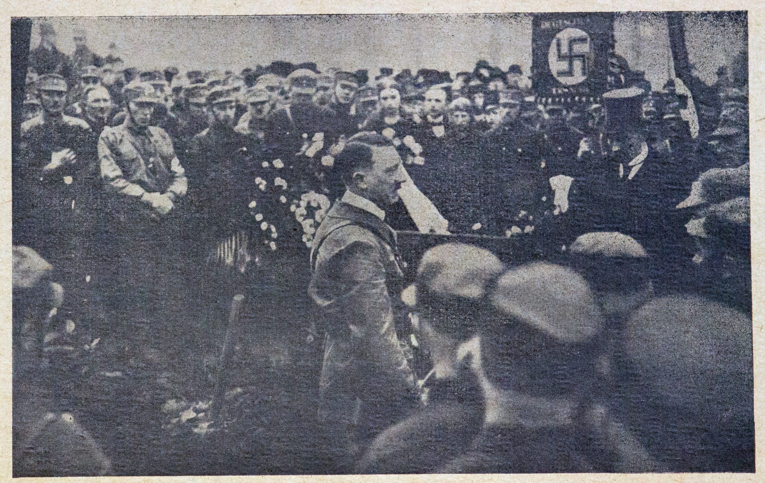 Auf der Schwarzweißfotografie ist in der Mitte Adolf Hitler abgebildet. Er ist umringt von zahlreichen Menschen: Frauen und Männer, entweder im Anzug gekleidet oder uniformiert. Sie zeigen bedrückte und ehrfürchtige Mienen. Im Hintergrund des Bildes ragt aus der Masse der Menschen eine Hakenkreuzfahne empor.